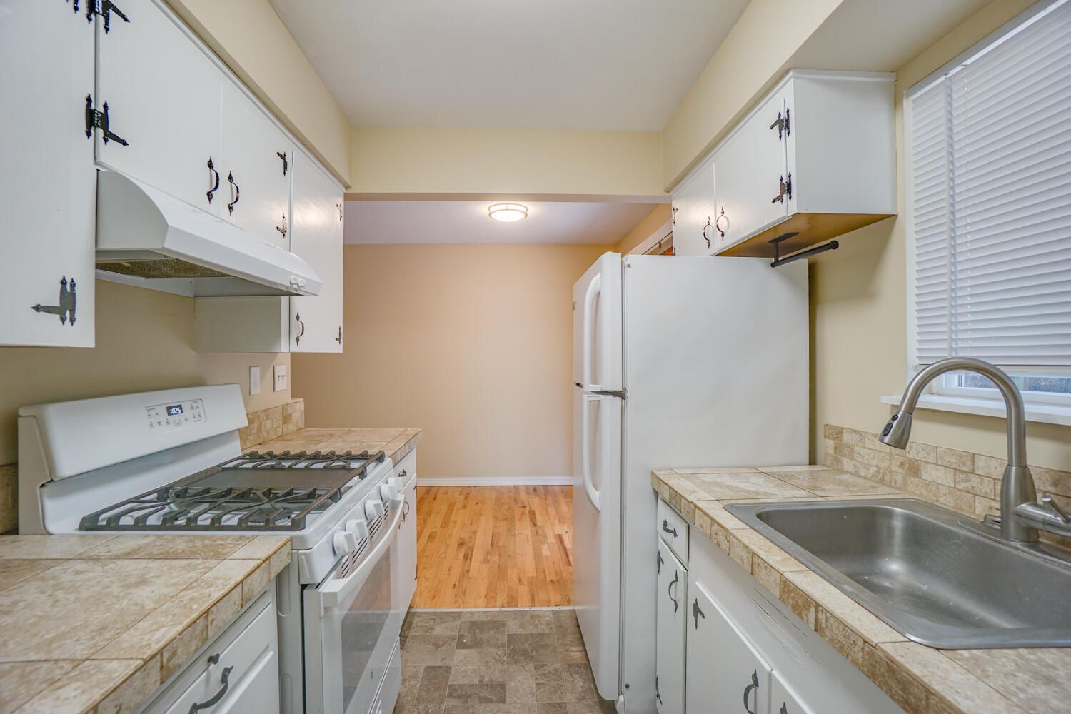 A kitchen with white cabinets , a stove , a refrigerator , and a sink.