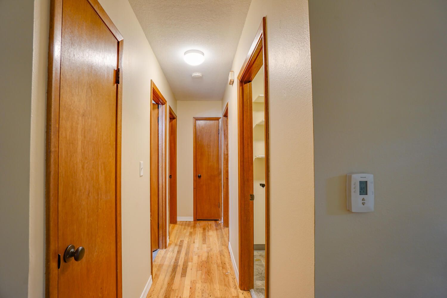 A long hallway with wooden doors and a thermostat on the wall.