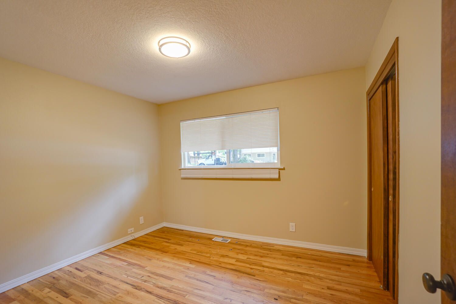 An empty bedroom with hardwood floors and a window.