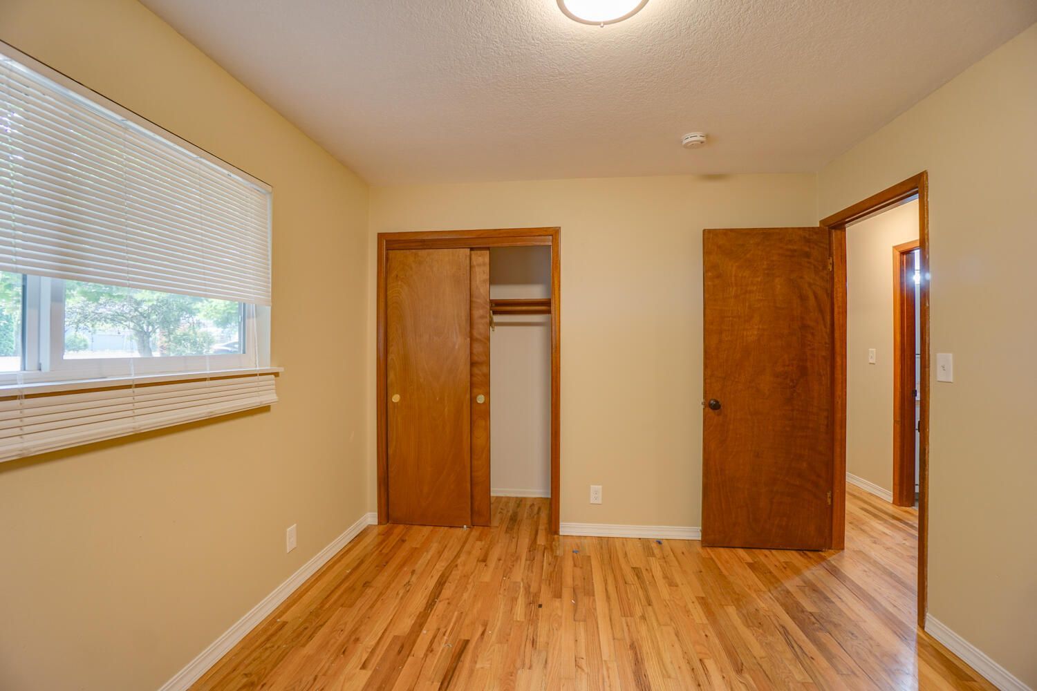 An empty bedroom with hardwood floors and a window.