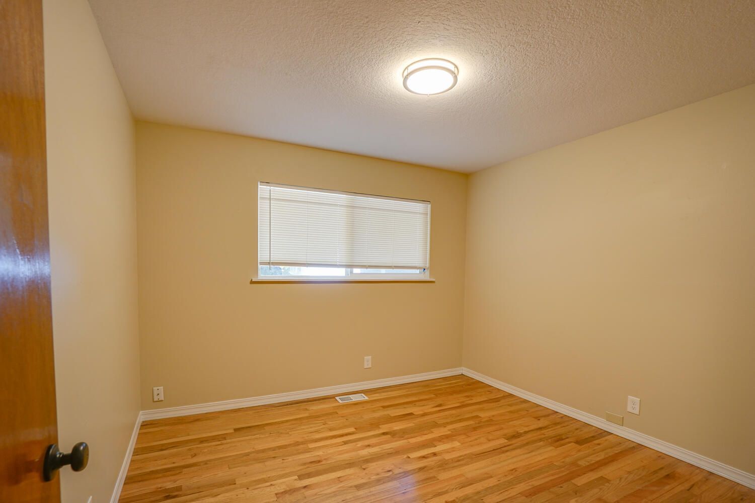 An empty bedroom with hardwood floors and a window.