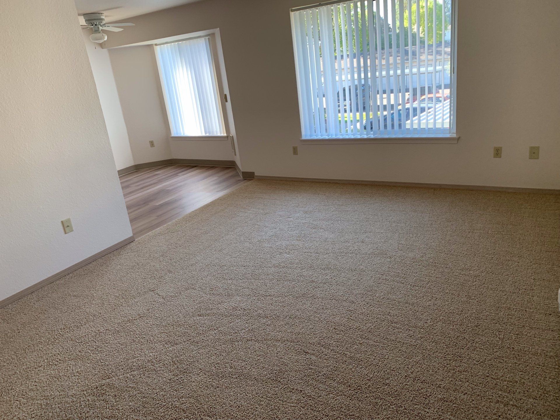 An empty living room with a large window and a ceiling fan.