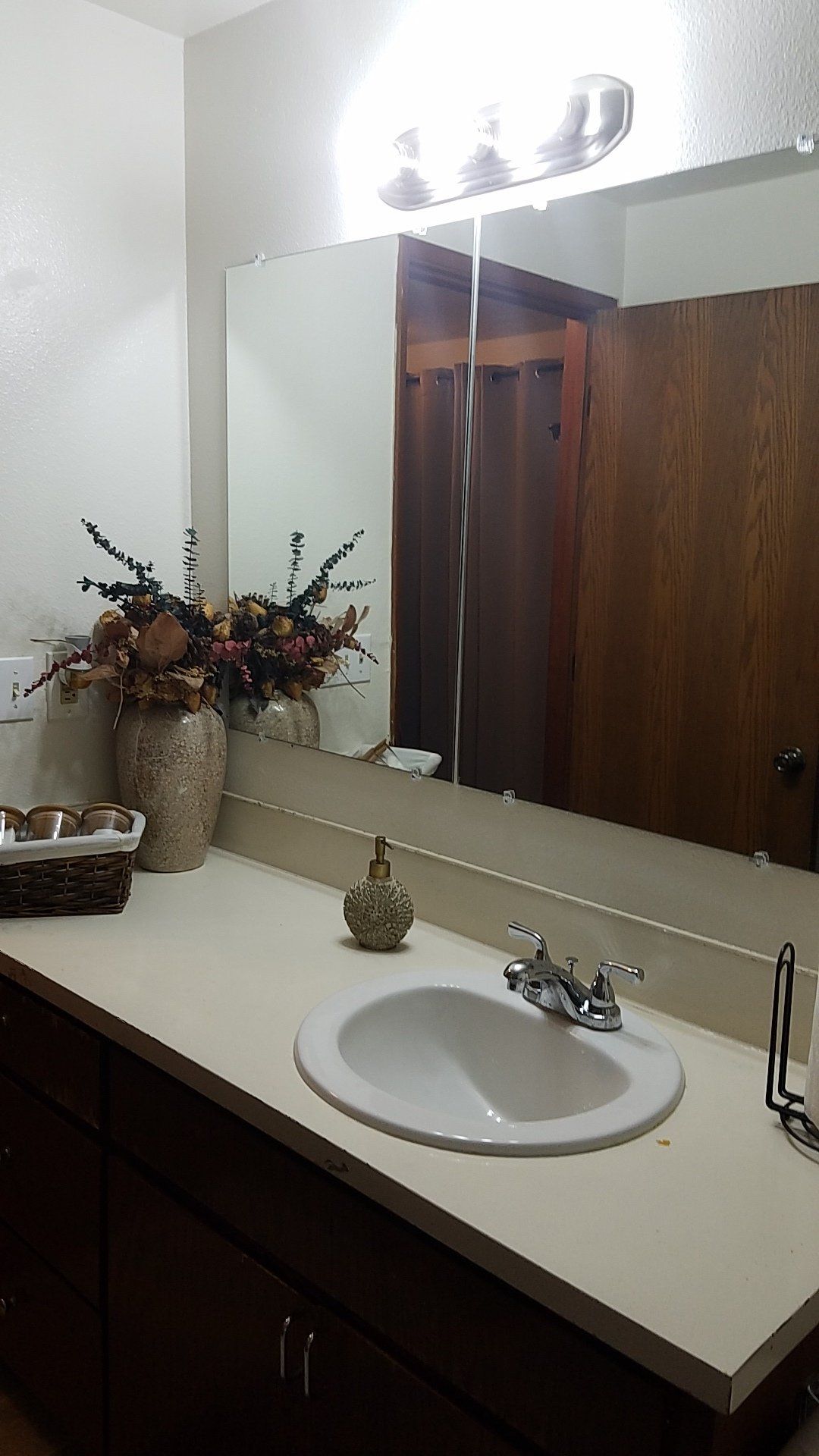 A bathroom with a sink , mirror and vase of flowers.