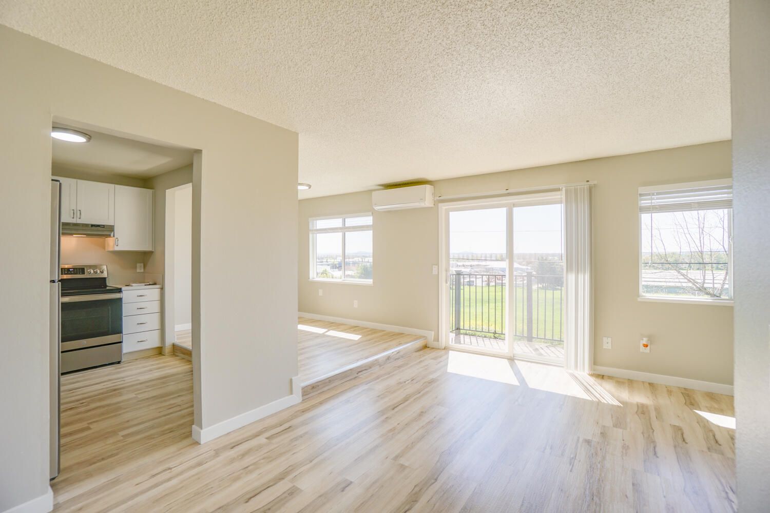 A living room with hardwood floors and sliding glass doors leading to a kitchen.