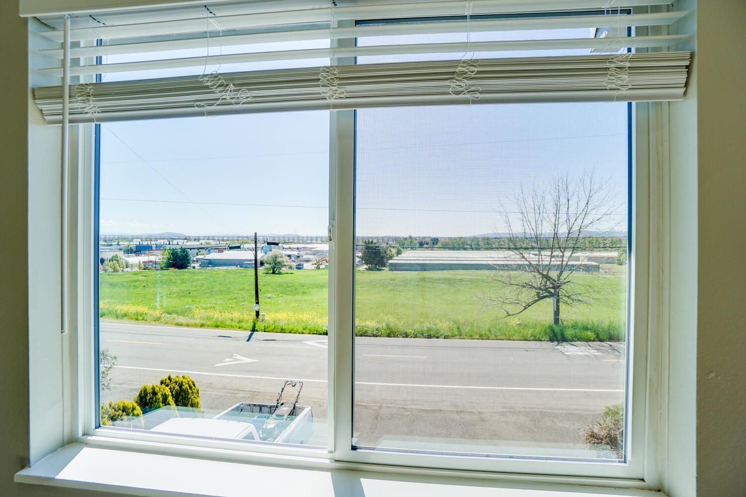 A window with blinds and a view of a field.