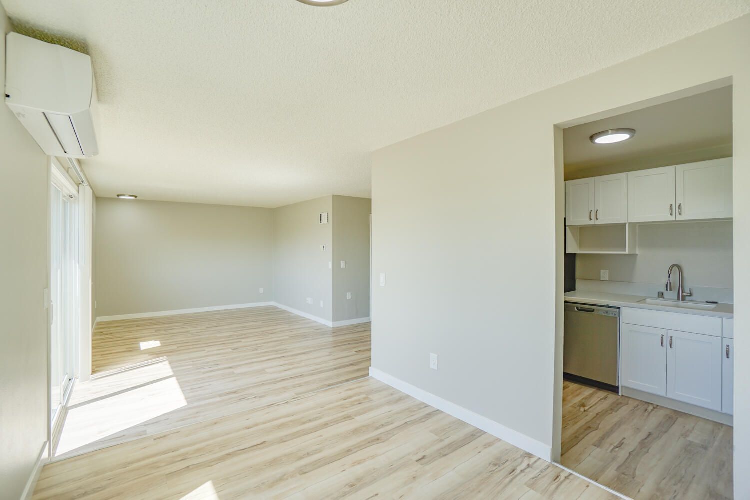 A living room with hardwood floors and a kitchen in the background.
