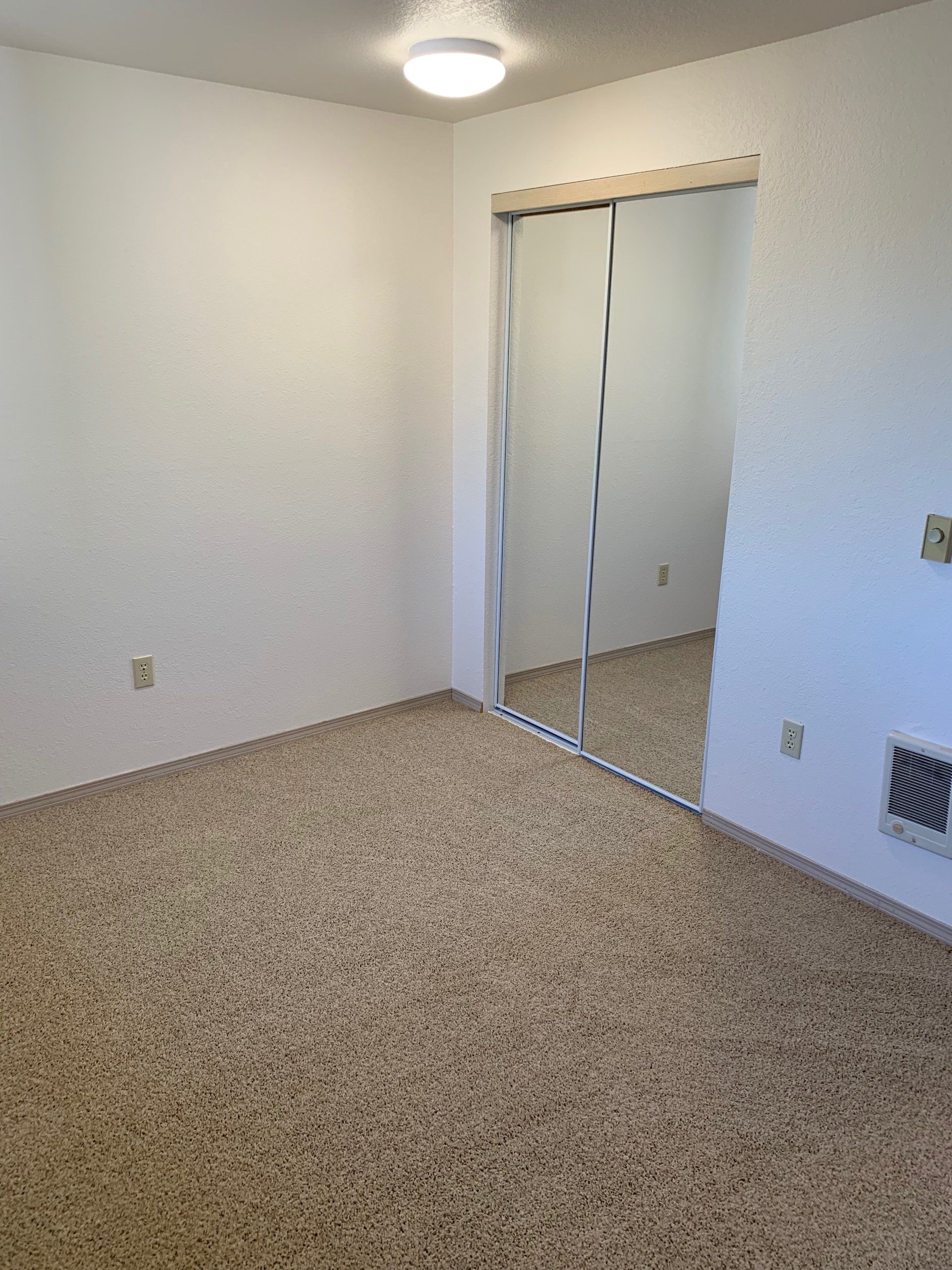 An empty bedroom with a large mirror in the closet.
