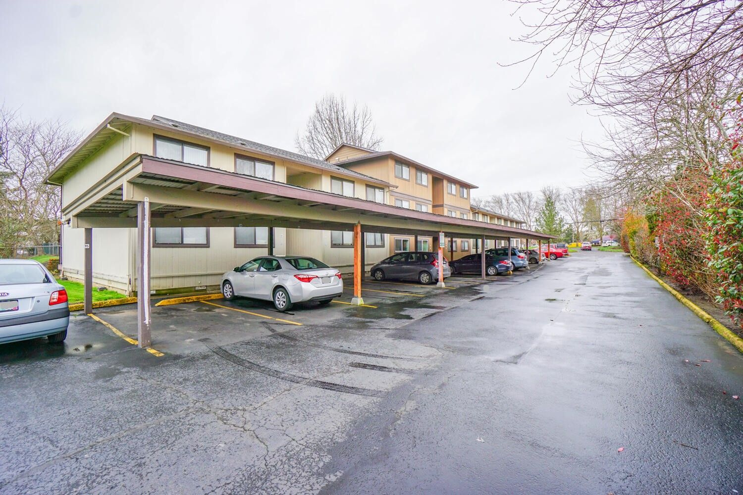 A parking lot with cars parked under a canopy in front of a building.
