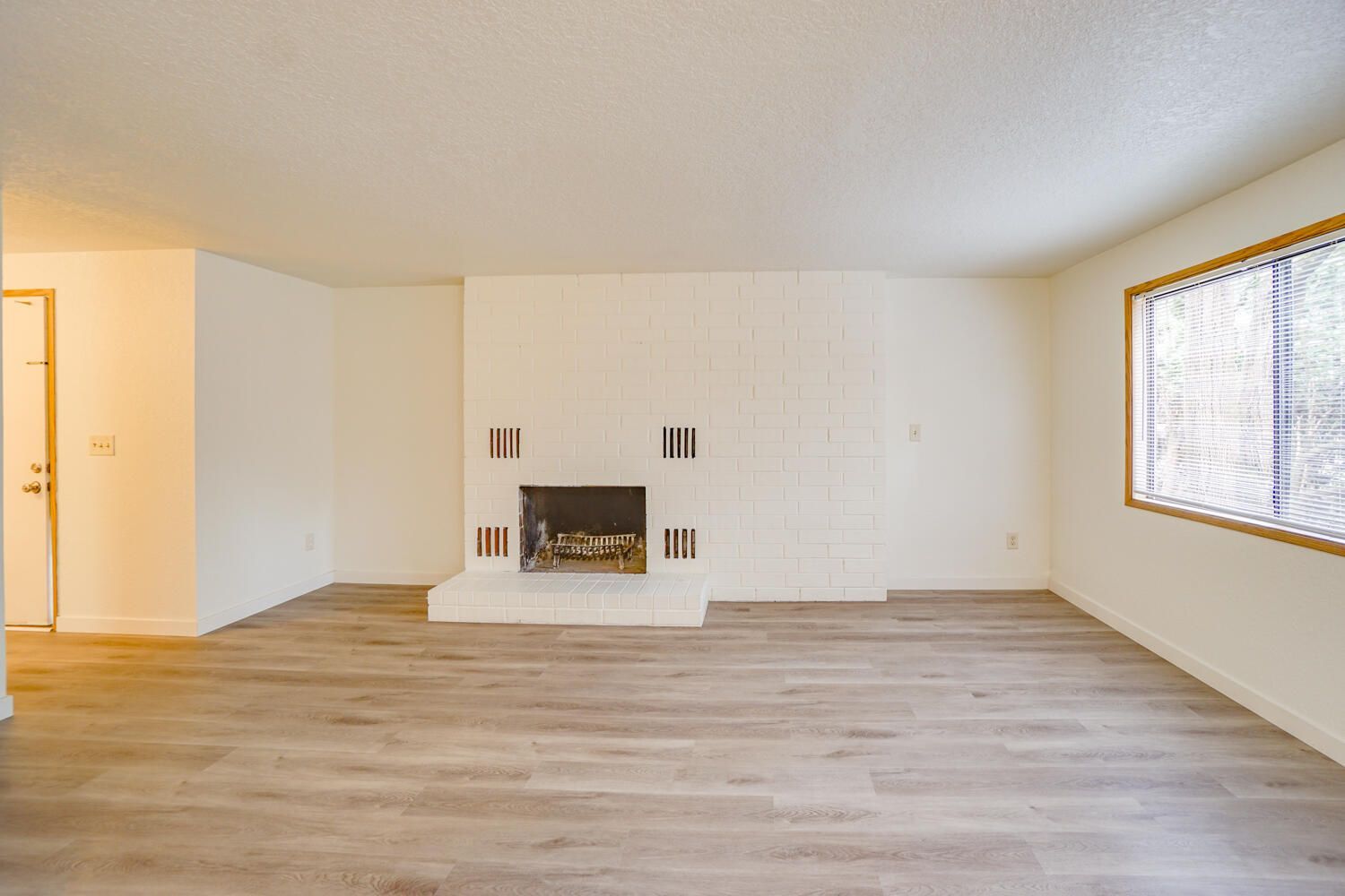 An empty living room with hardwood floors and a fireplace.