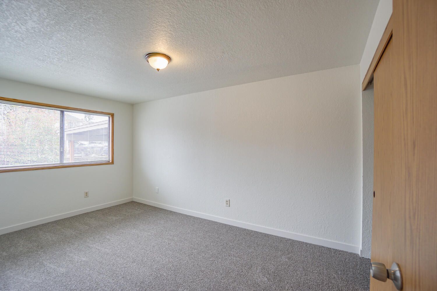 An empty bedroom with a carpeted floor and a window.