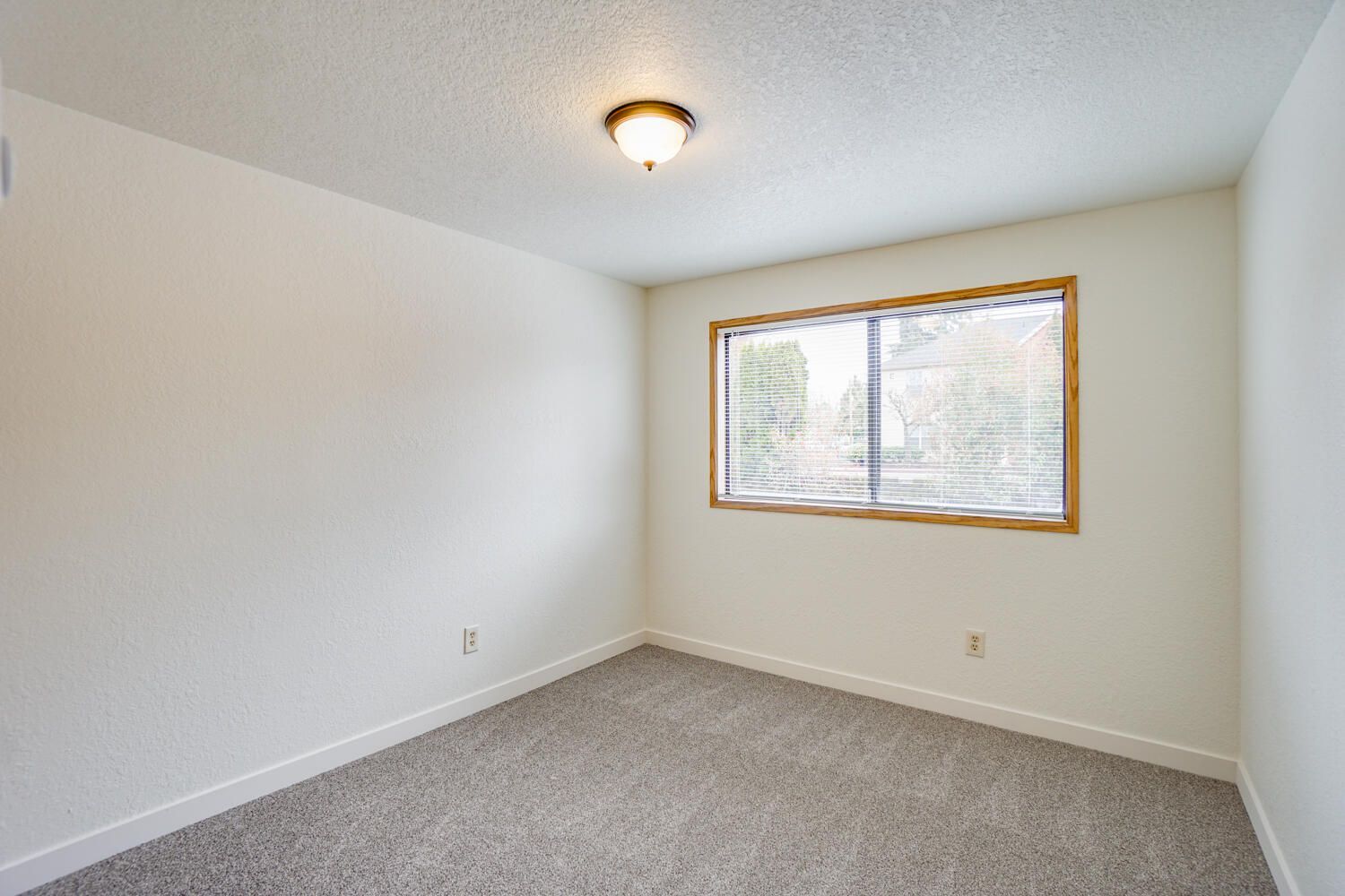 An empty bedroom with a window and a ceiling light.