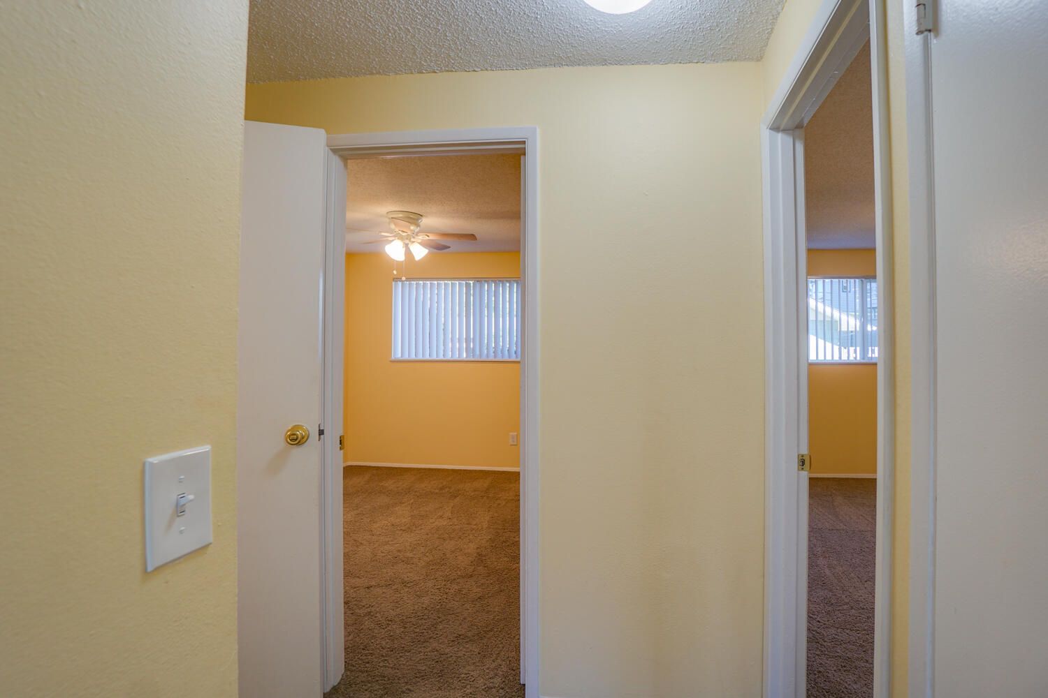 A hallway with yellow walls and white doors leading to a bedroom.
