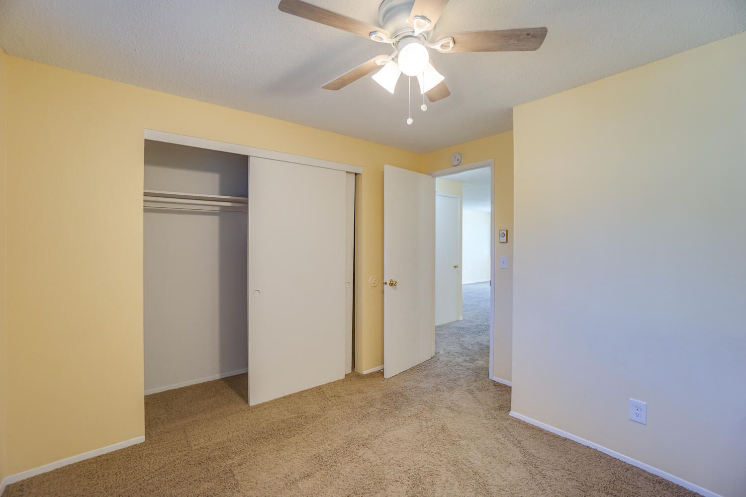 An empty bedroom with a ceiling fan and a closet.