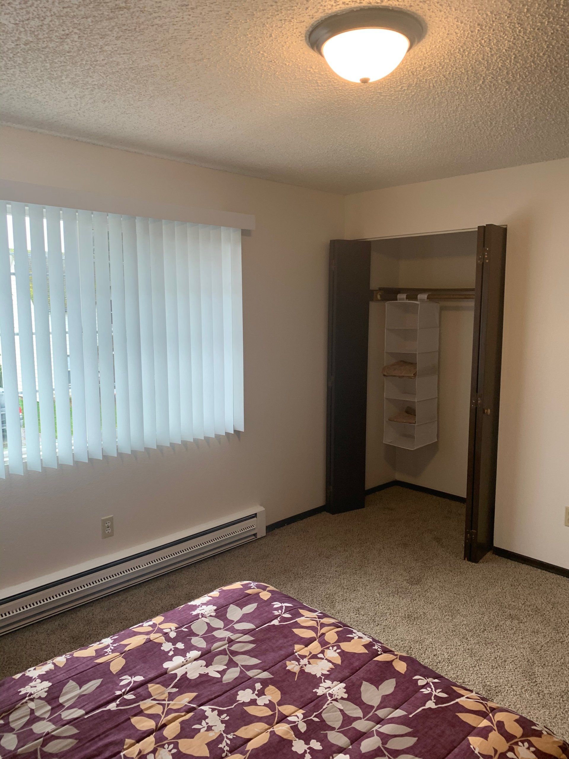 A bedroom with a bed and a window with blinds