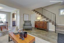 A living room with a coffee table , chair , dresser and stairs.