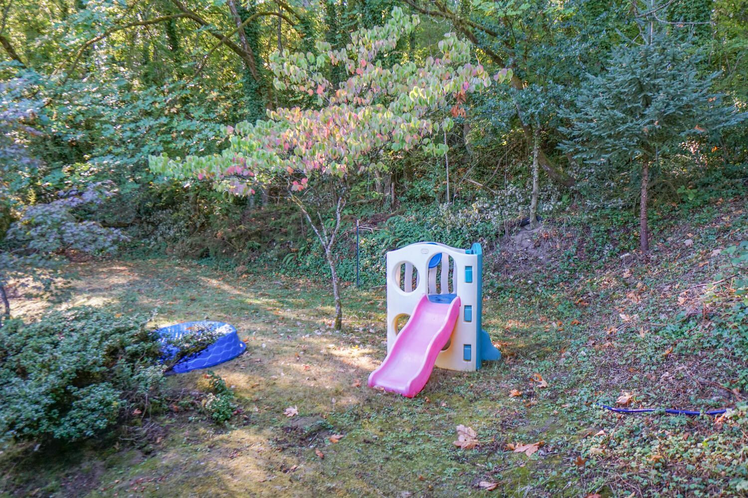 Play structure with pink slide on grassy hill surrounded by trees.