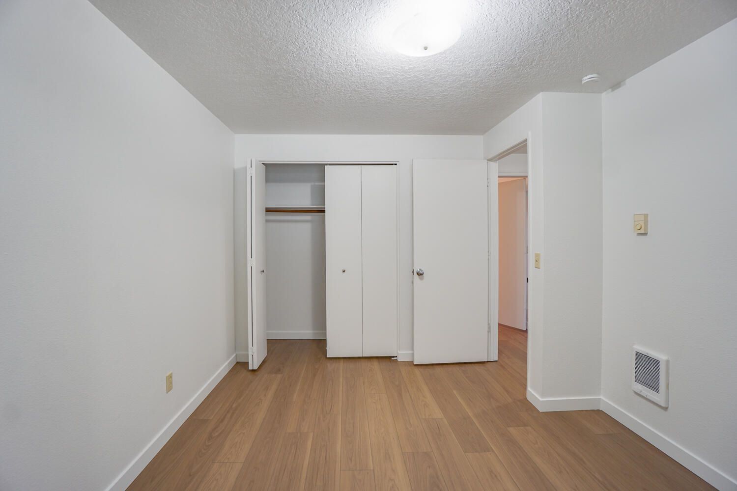 Empty white bedroom with wooden floors, closet, and doorway.