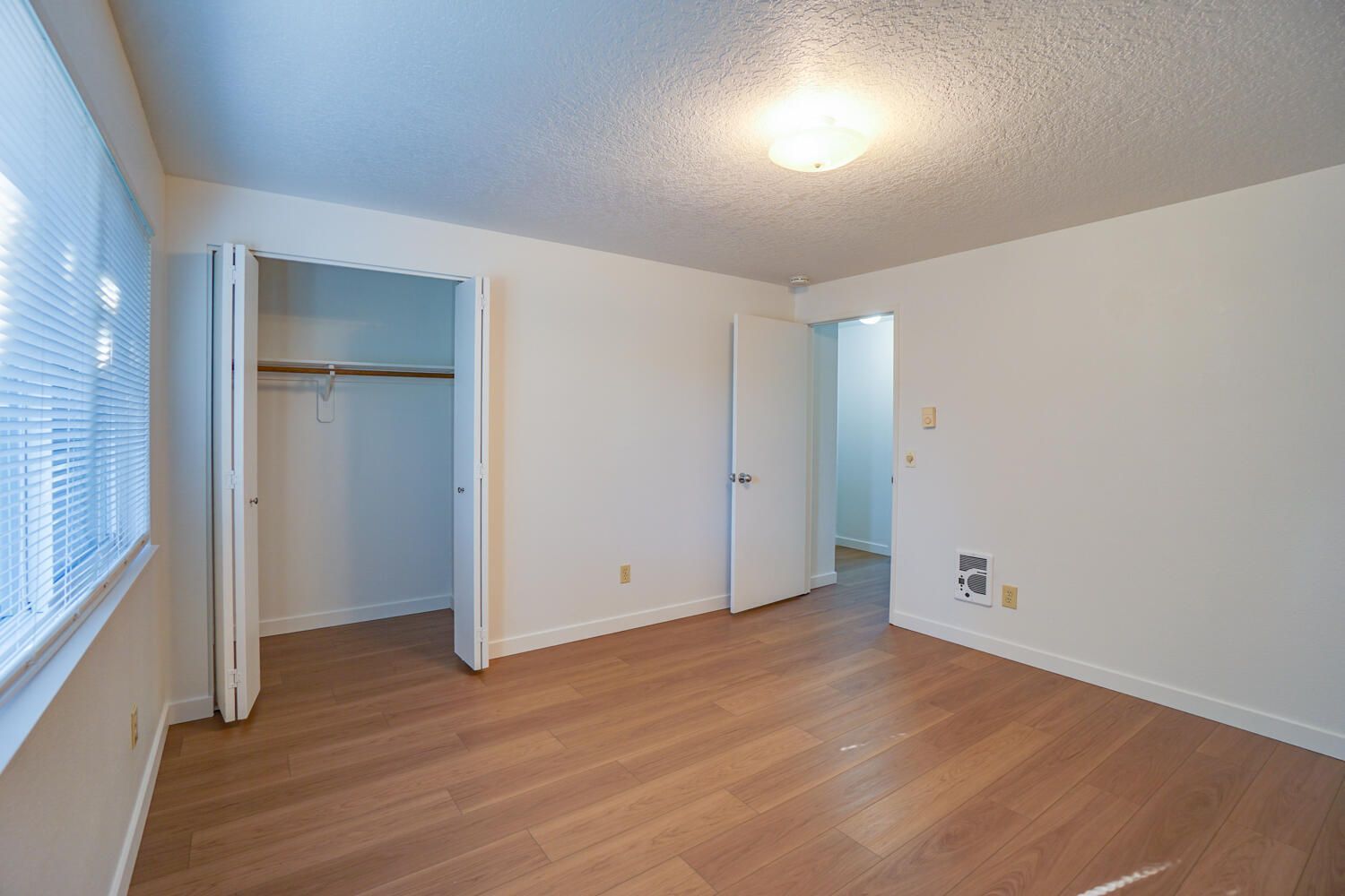Empty bedroom with wooden floors, closet, and door leading to hallway.