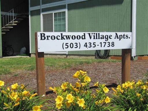 A sign for brockwood village apartments is surrounded by yellow flowers