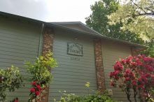 A house with a sign on the side of it and a bush with red flowers in front of it.