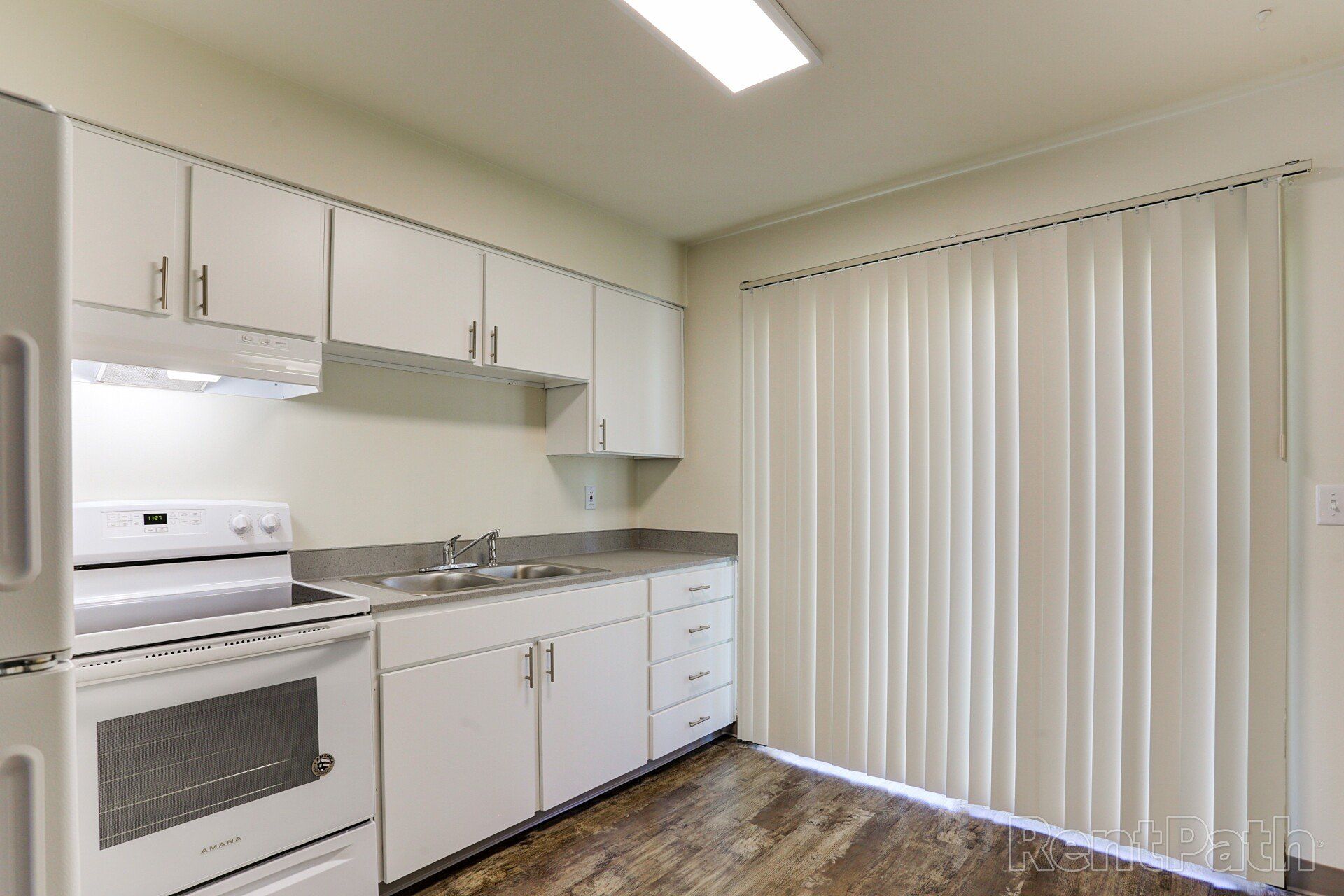 A kitchen with white cabinets , a stove , a refrigerator , and a sink.