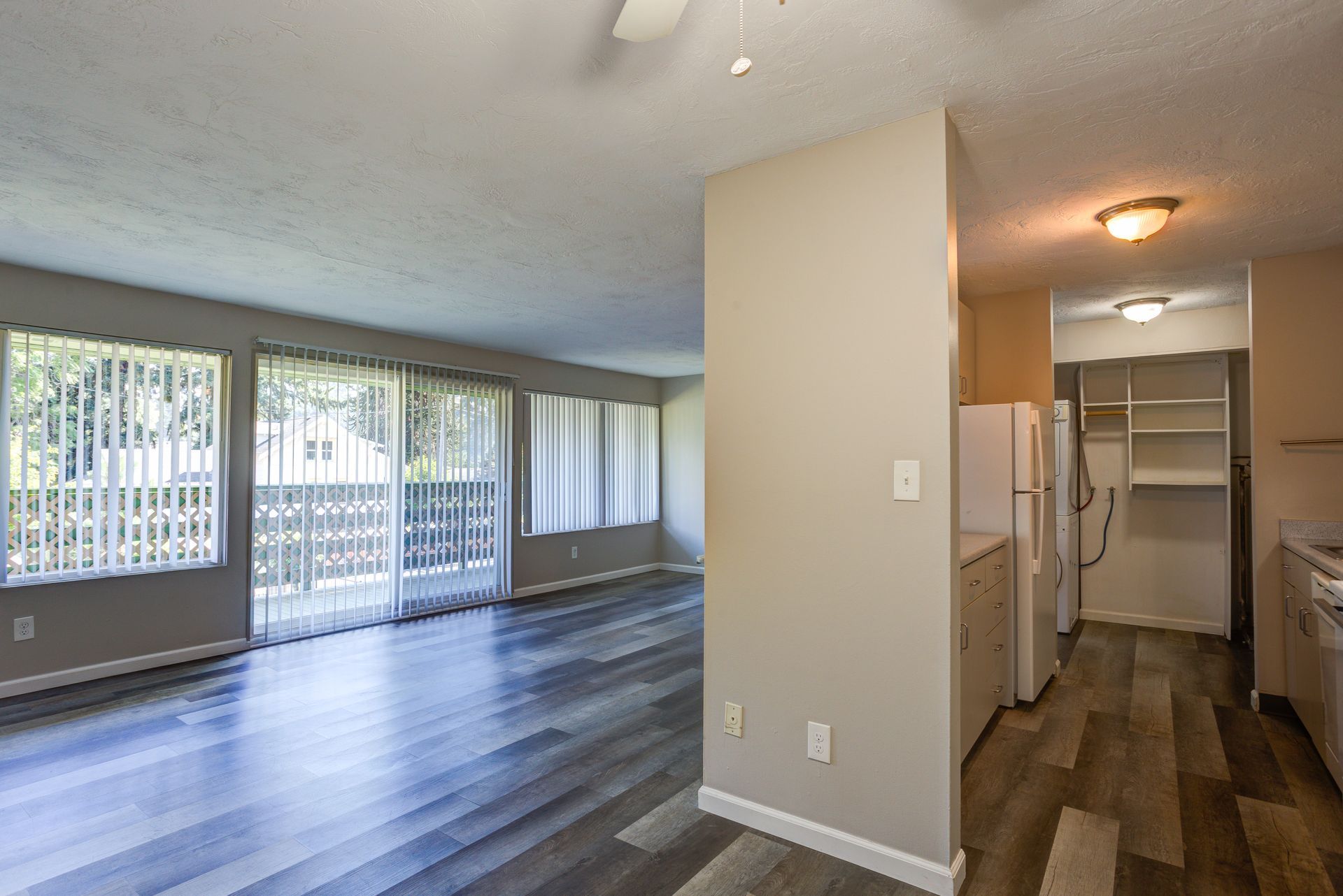 A living room with hardwood floors and sliding glass doors leading to a kitchen.
