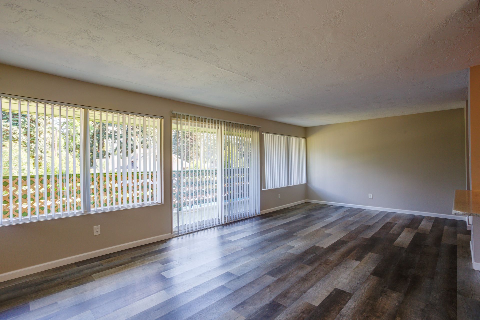 An empty living room with hardwood floors and sliding glass doors.