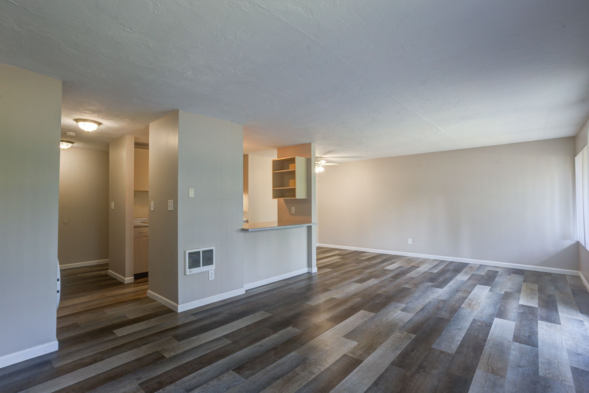 An empty living room with hardwood floors and a kitchen in the background.