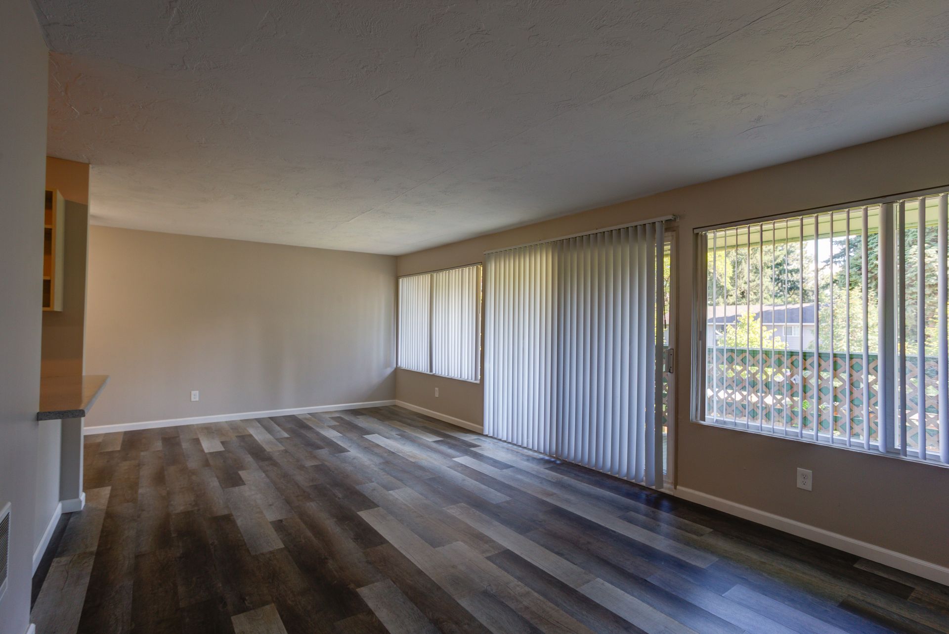 An empty living room with hardwood floors and sliding glass doors.