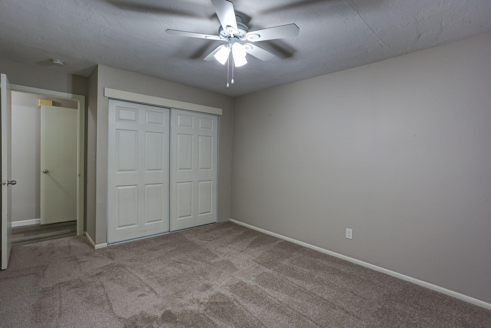 An empty bedroom with a ceiling fan and sliding doors.