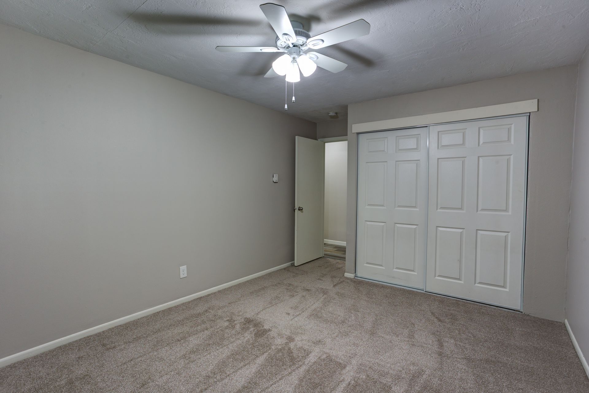 An empty bedroom with a ceiling fan and a closet.