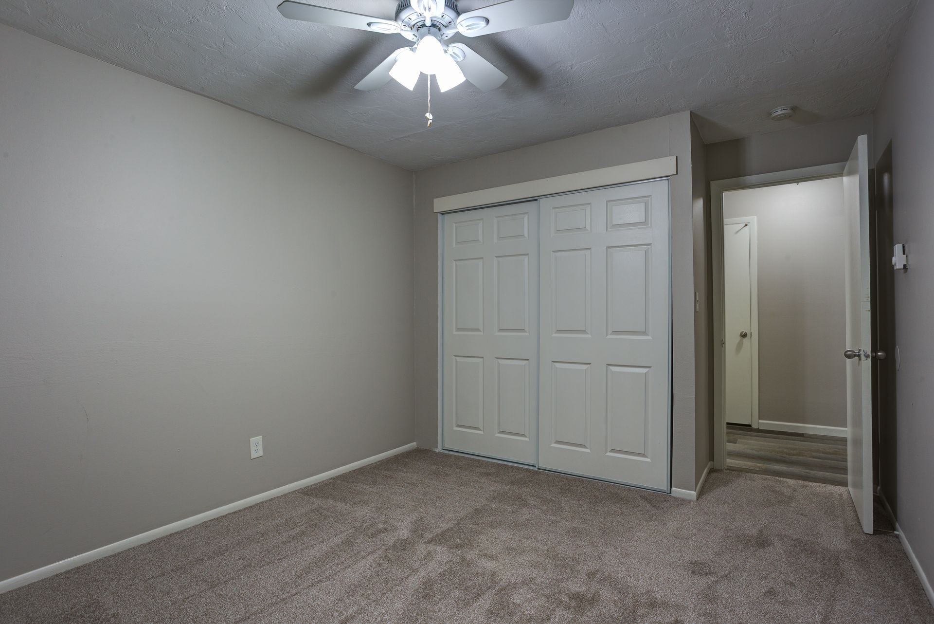 An empty bedroom with a ceiling fan and a large closet.