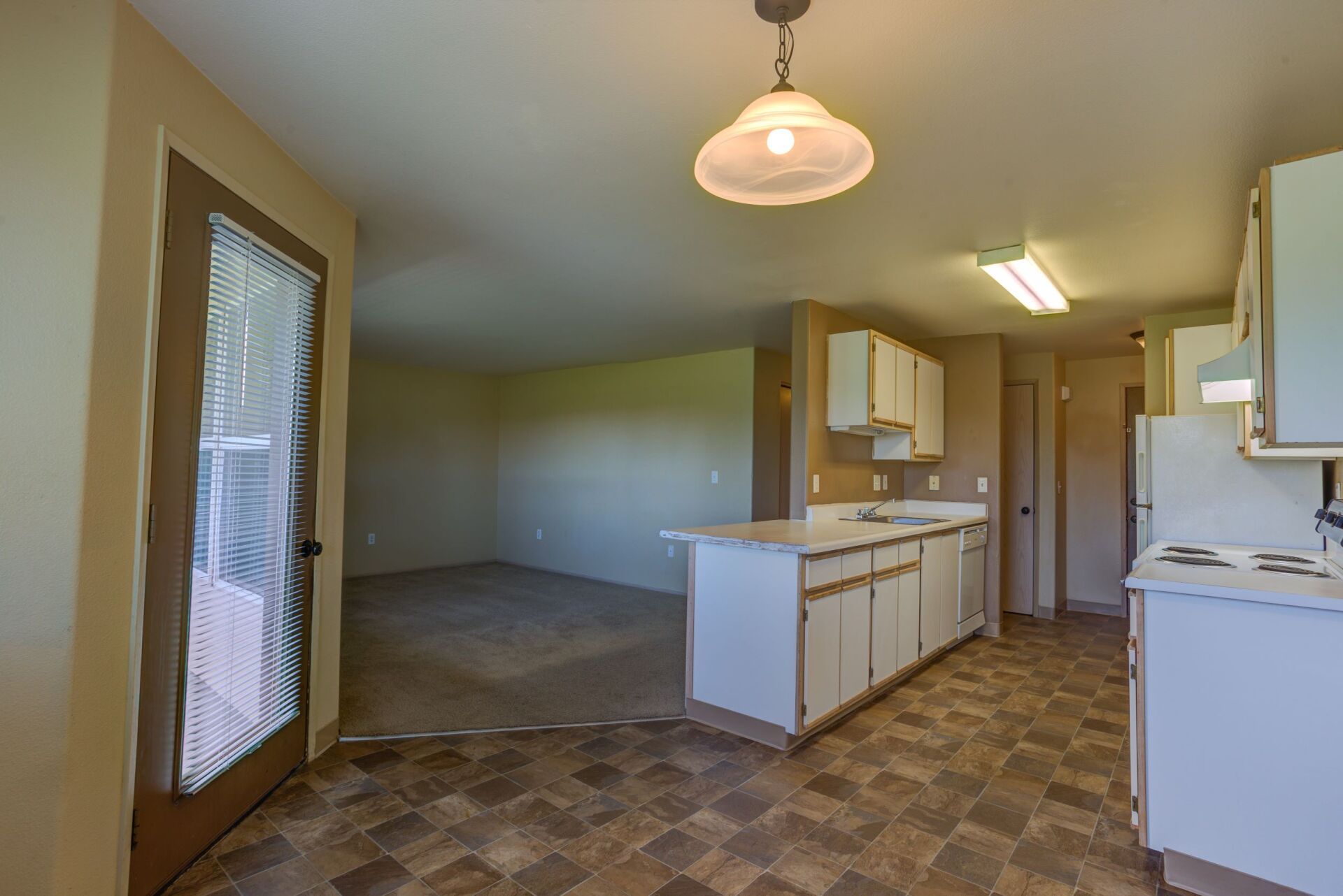 A kitchen with a stove , sink , cabinets and a sliding glass door.