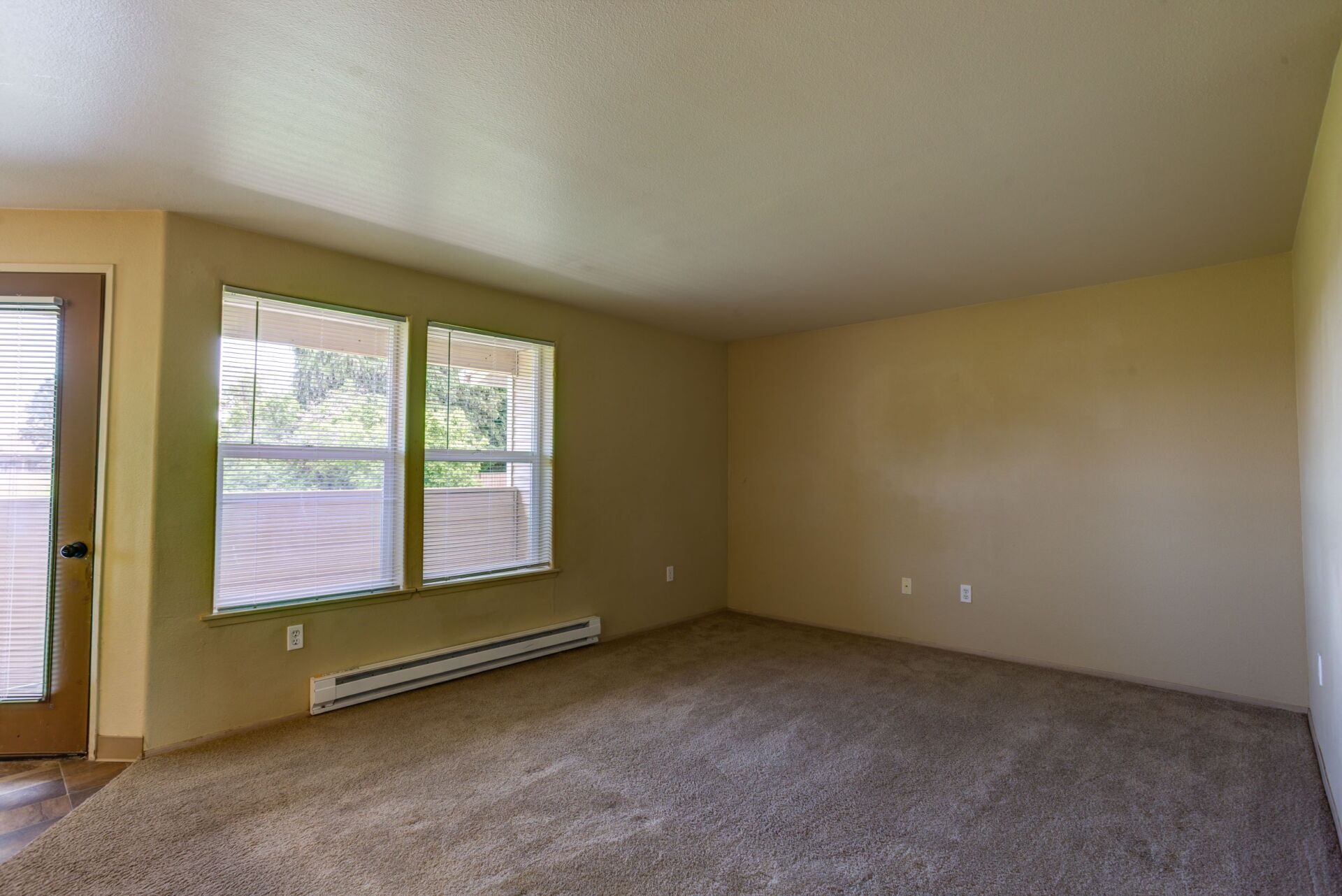 An empty living room with two windows and a sliding glass door.