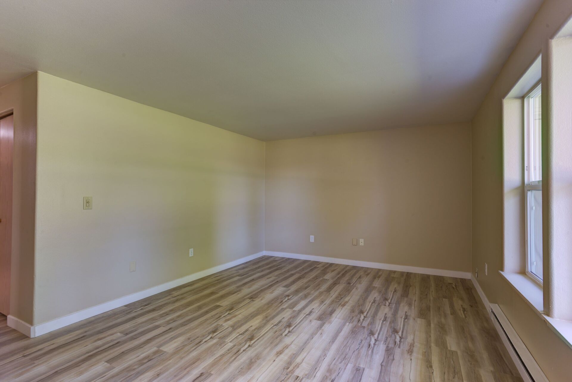 An empty living room with hardwood floors and two windows.
