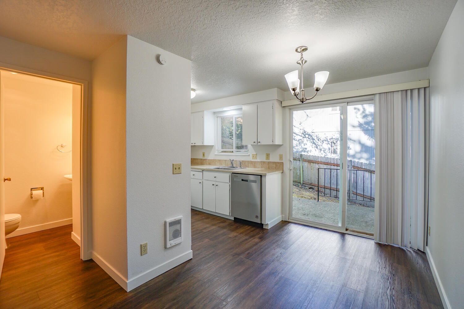 Interior view: Kitchen with white cabinets, dishwasher, sliding glass door to small patio, dark wood floors.