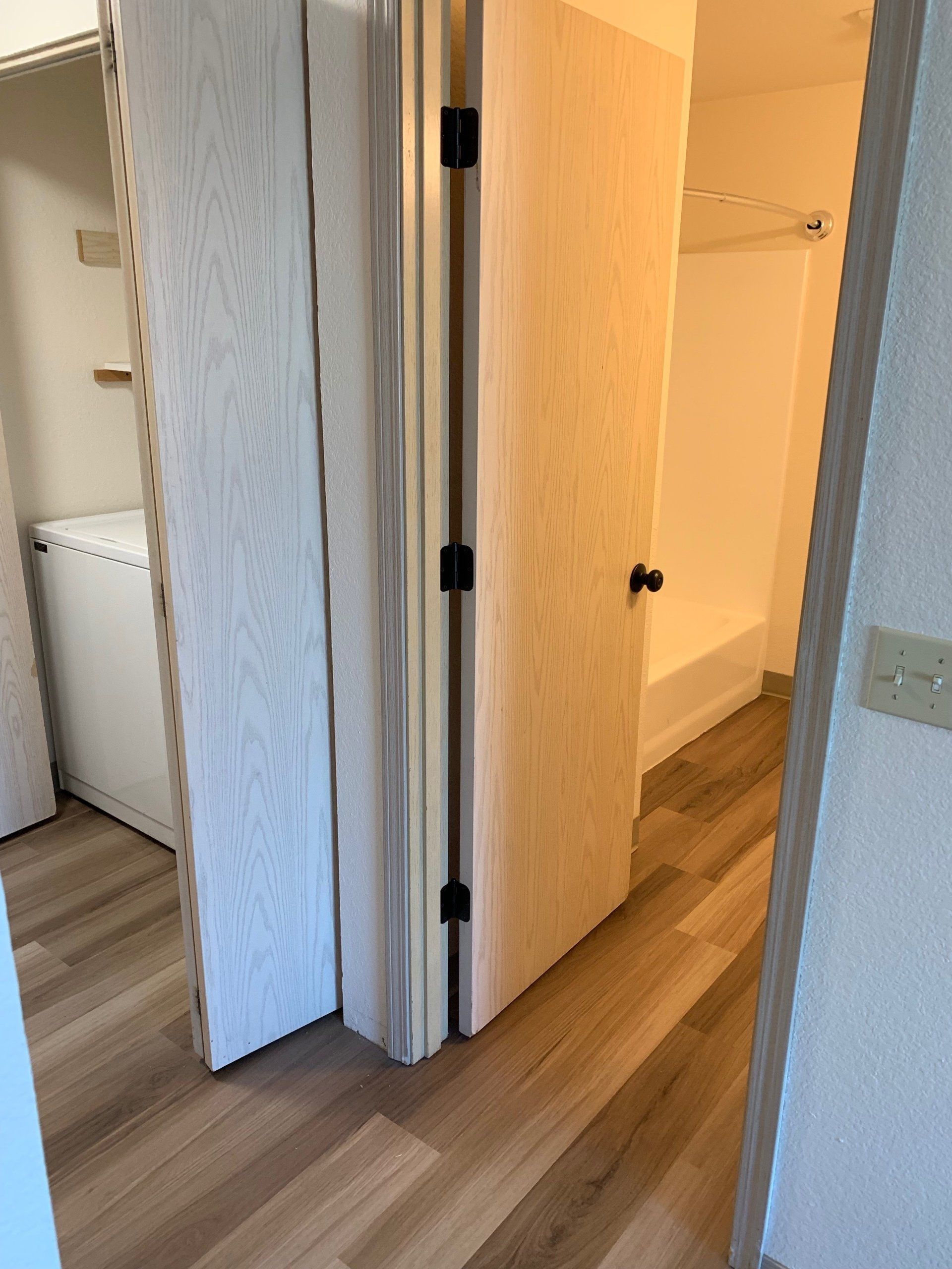A hallway with hardwood floors leading to a laundry room and a bathroom.