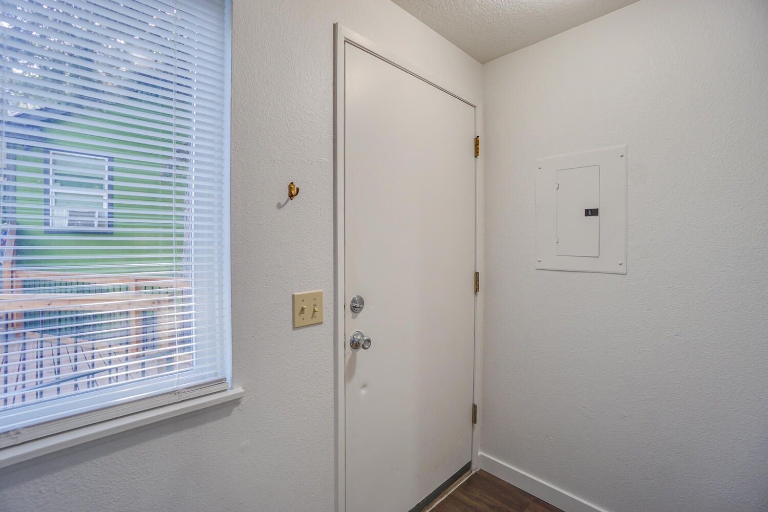 Entryway with white door, window with blinds, electrical panel, light switch, and coat hooks.
