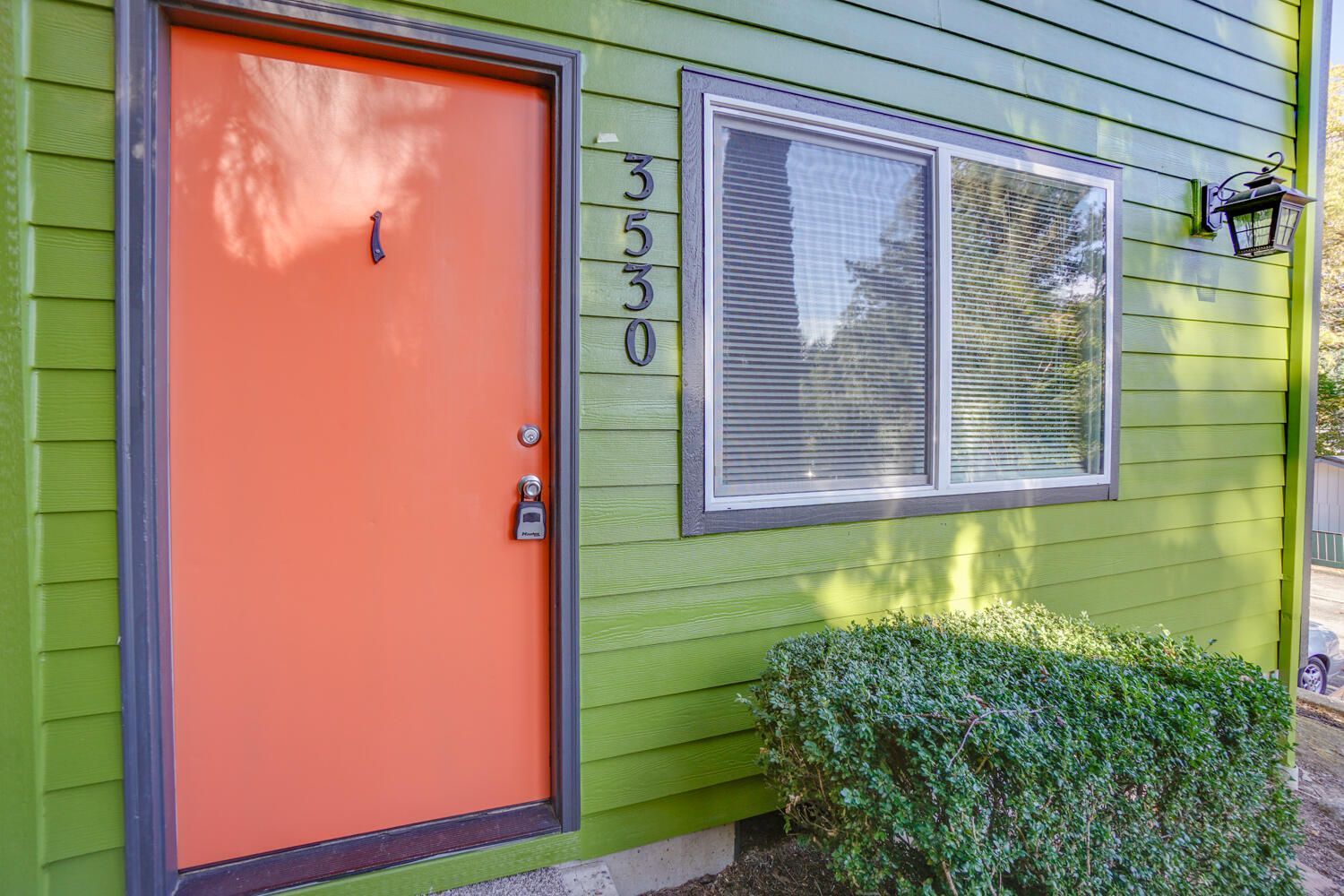 Orange door with house number 3530 on a green exterior with a window and small bush.