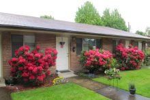 A brick apartment building with red flowers in front of it.