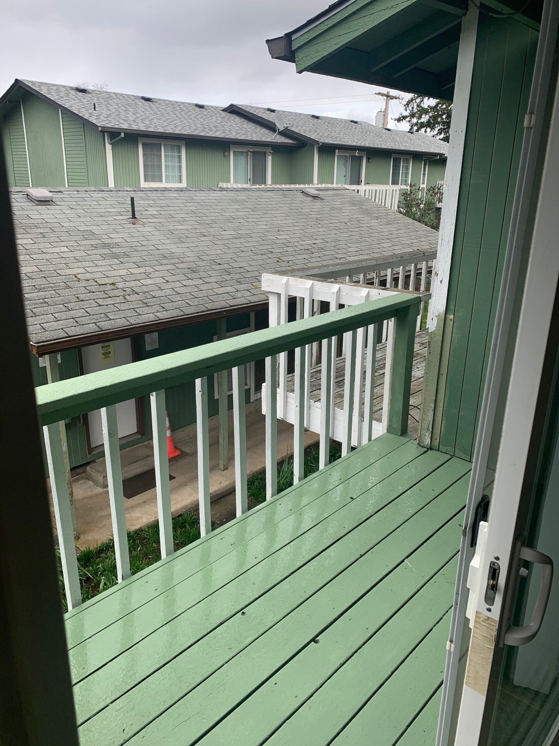 A green deck with a white railing and a view of a building.