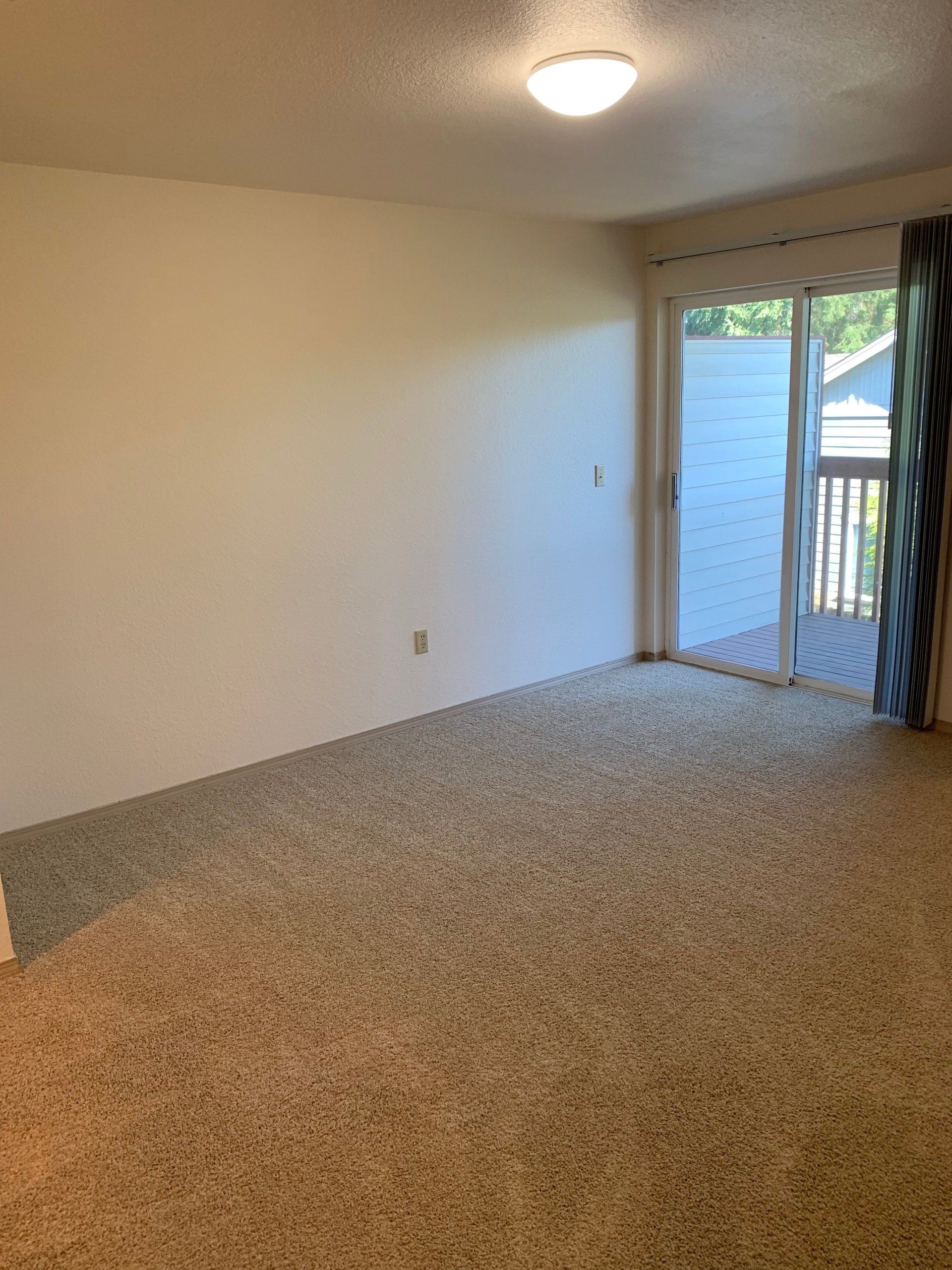 An empty living room with a sliding glass door and a balcony.