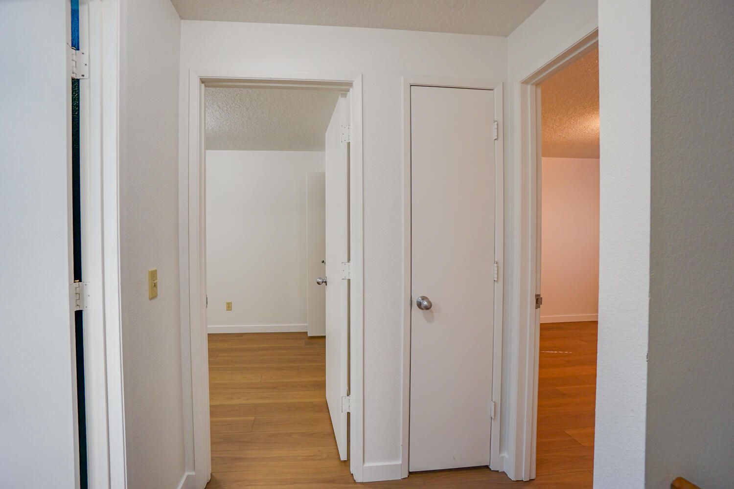 Hallway with three white doorways leading to rooms with light wooden floors.