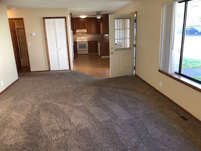 An empty living room with a carpeted floor and a window