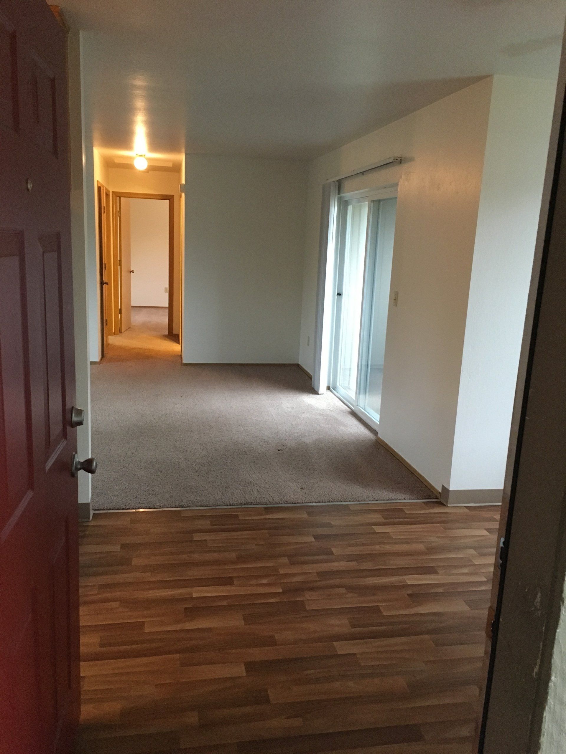 An empty living room with hardwood floors and a red door