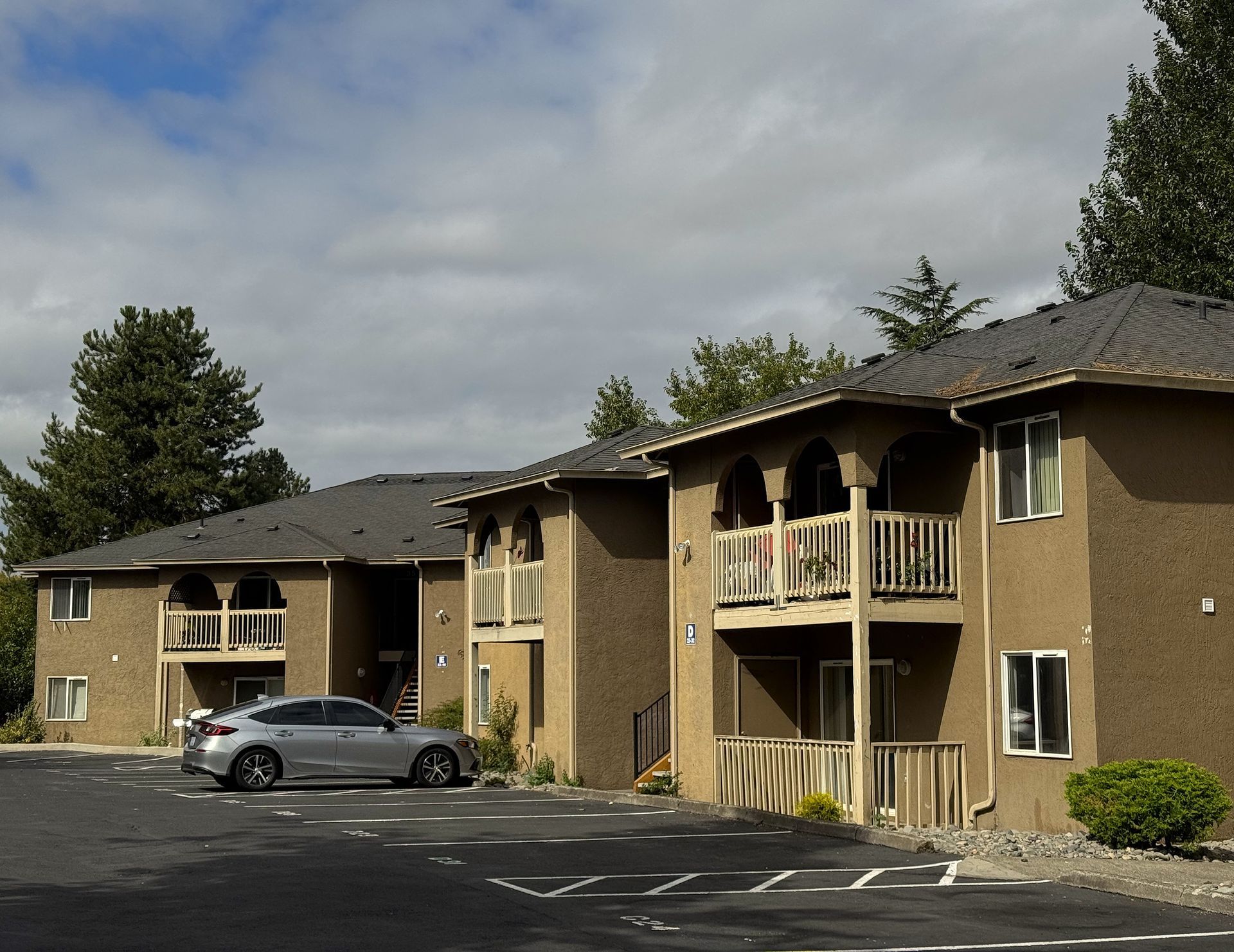Apartment complex with two-story buildings. Gray car parked in front. Overcast sky.