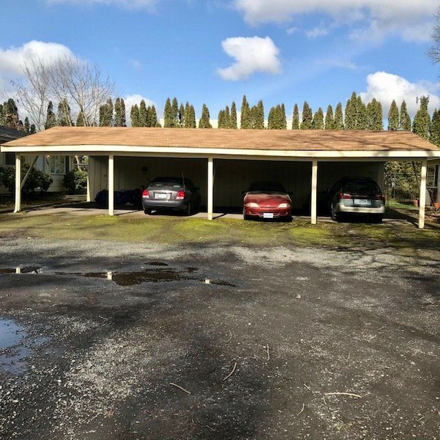 Three cars are parked under a carport with trees in the background