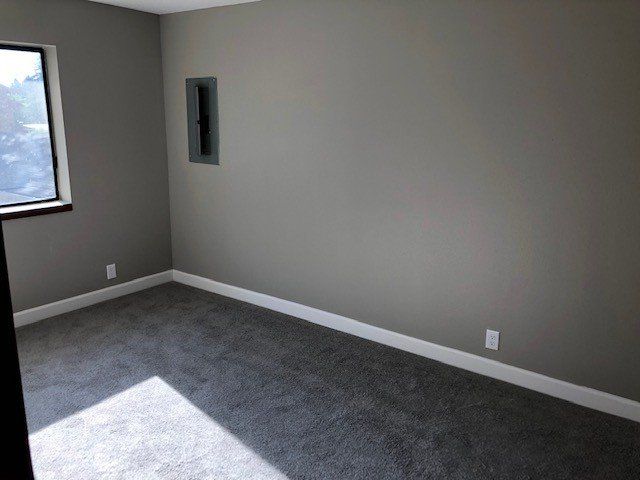 An empty room with a window and a gray carpet.