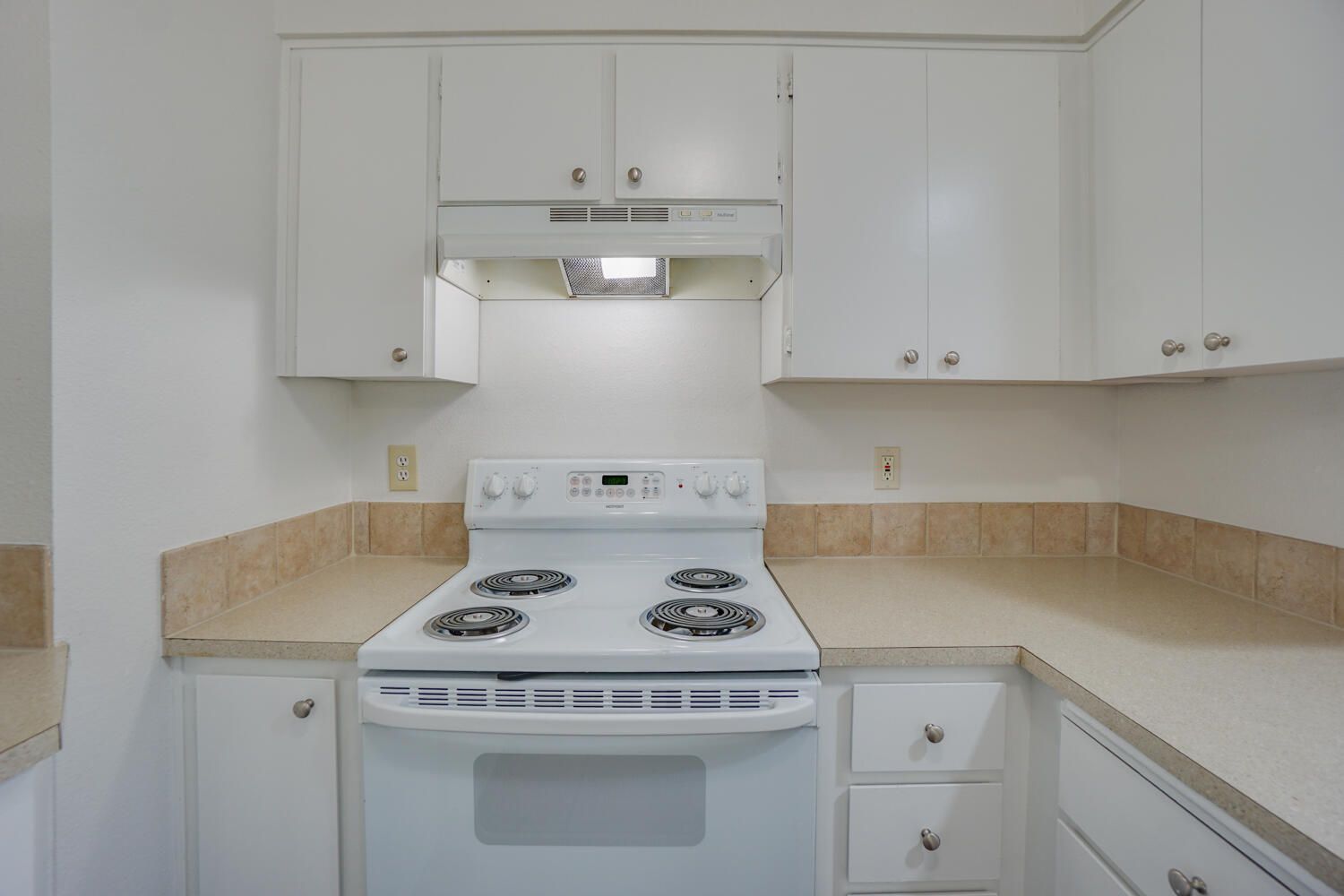 White kitchen with stove, cabinets, and light-colored countertops.