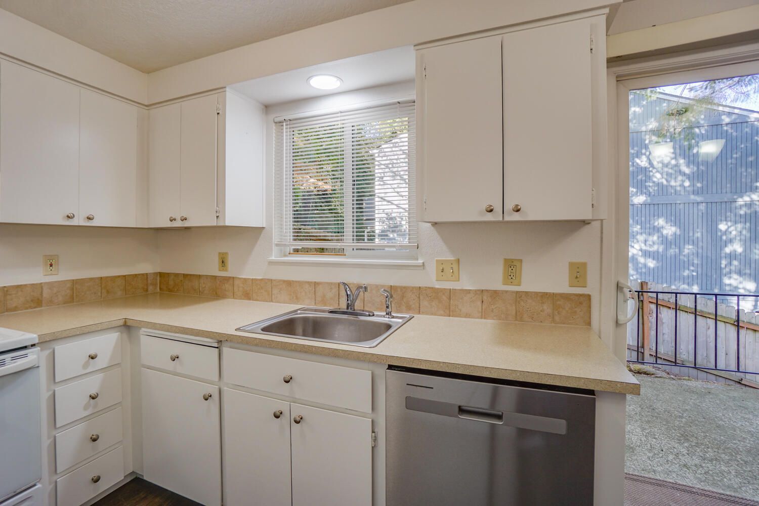 White kitchen with cabinets, countertops, and appliances. Includes a window and door to an outdoor space.